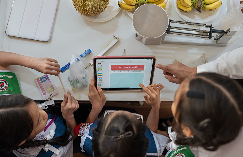 Drie basisschoolleerlingen rond een iPad werken samen aan de presentatie van een natuurkundeproject.