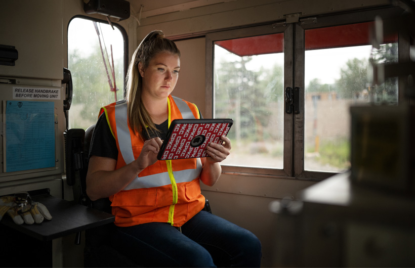 En jernbanearbeider sitter inne i et stillestående tog og sjekker noe på en iPad