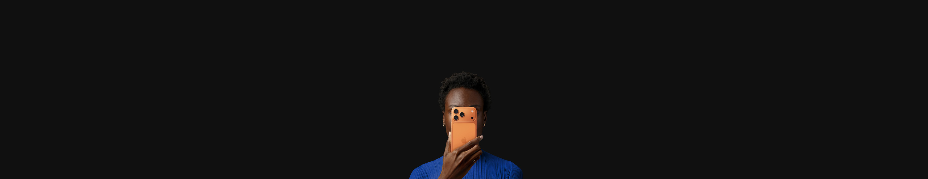 A person holds iPhone 17 Pro in front of their face, back exterior facing outward, Cosmic Orange colour.