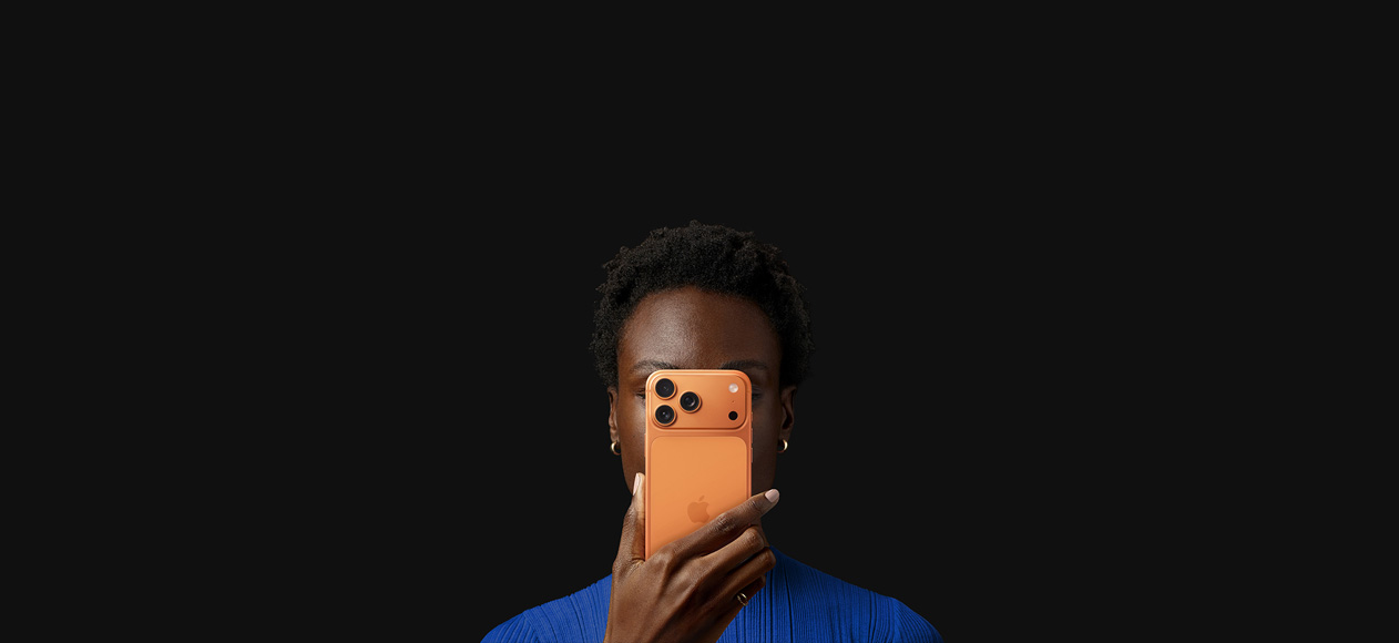 Une personne tient un iPhone 17 Pro devant son visage, face arrière tournée vers l’extérieur, coloris Orange Cosmique.