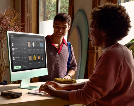 Heller Raum mit zwei Personen. Eine Frau nutzt einen iMac mit einem Display mit Nanotexturglas, während ein Mann daneben sitzt